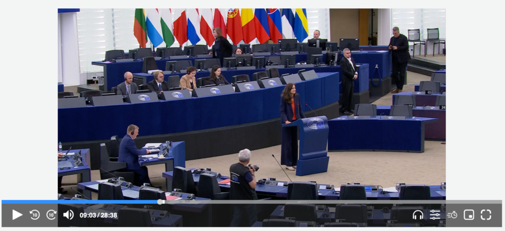 Screenshot of a streaming video player showing a female speaker in the European Parliament